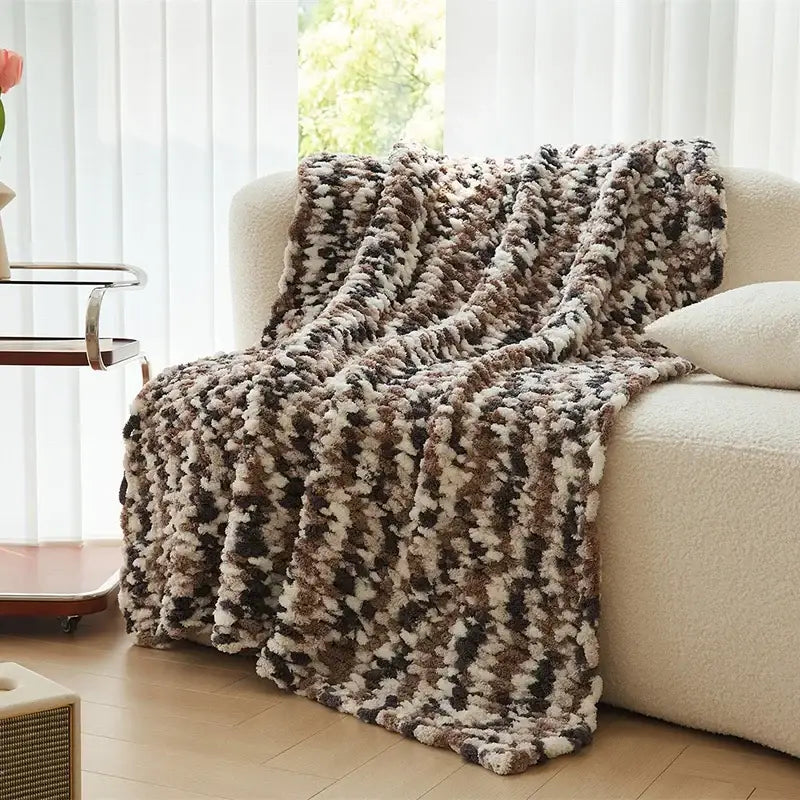 A plush chunky knit jacquard blanket throw in beige brown and black draped over a cream sofa for living room decor