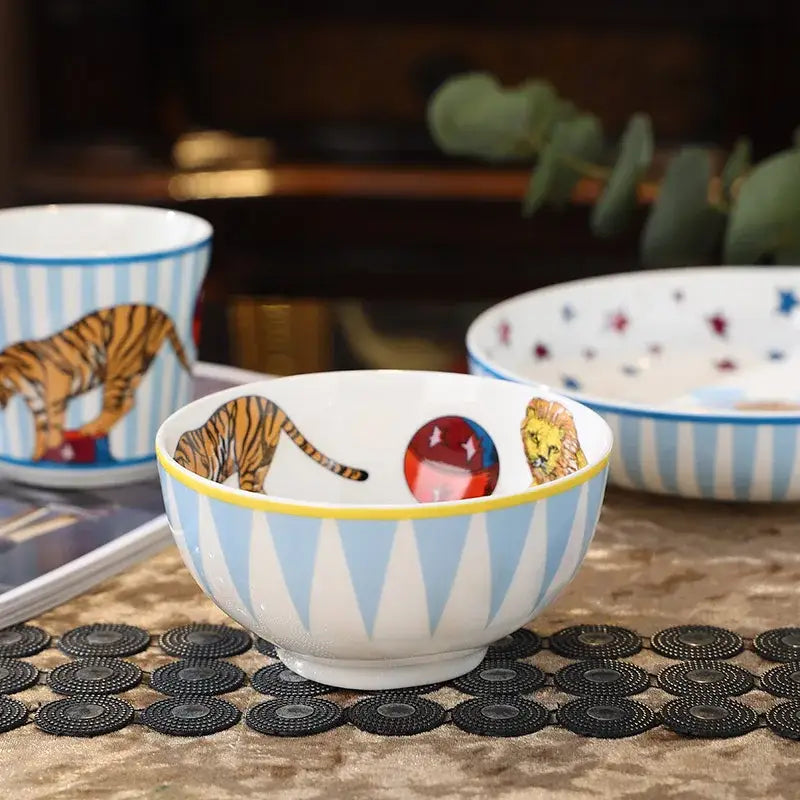 A white ceramic bowl with light blue and yellow stripes featuring tiger lion and ball design from decorbites circus troup tableware set