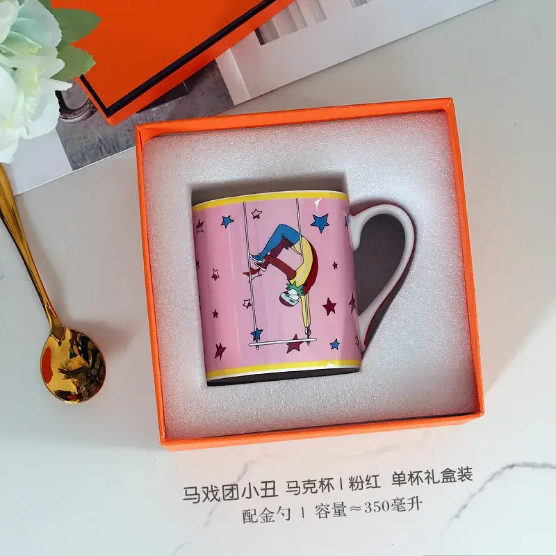 Pink ceramic mug with cartoon acrobat design and yellow trim in orange box from decorbites circus troup kids tableware set