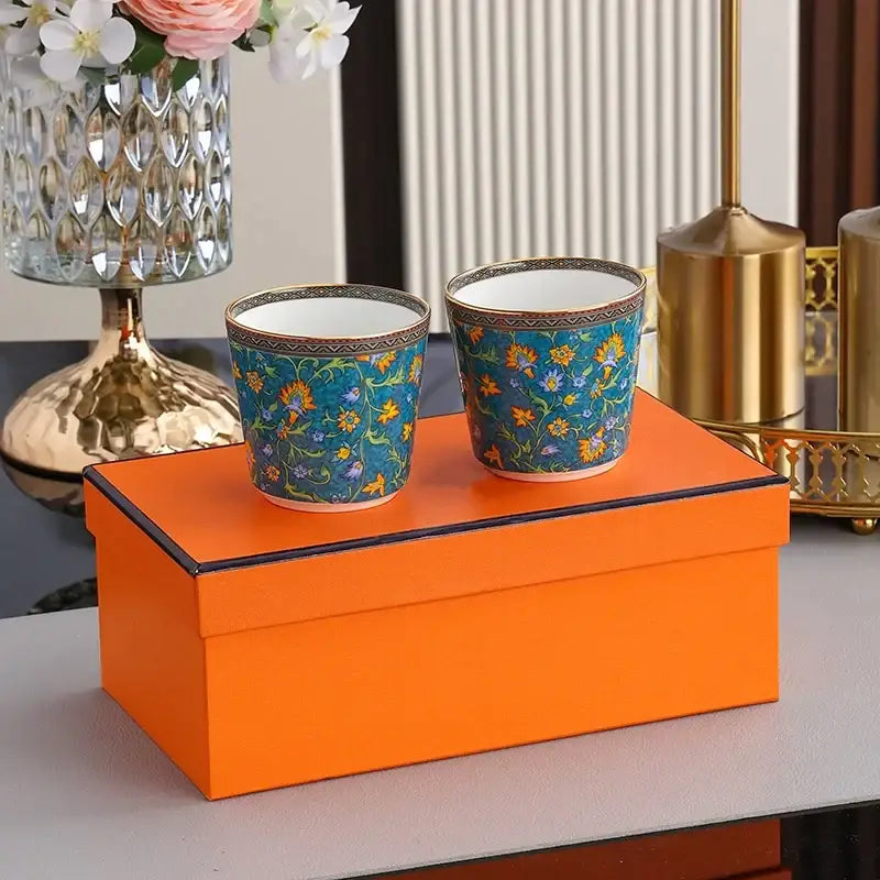 Two matching ceramic tea cups with vibrant blue base and floral patterns on orange gift box from decorbites circus troup kids tableware set