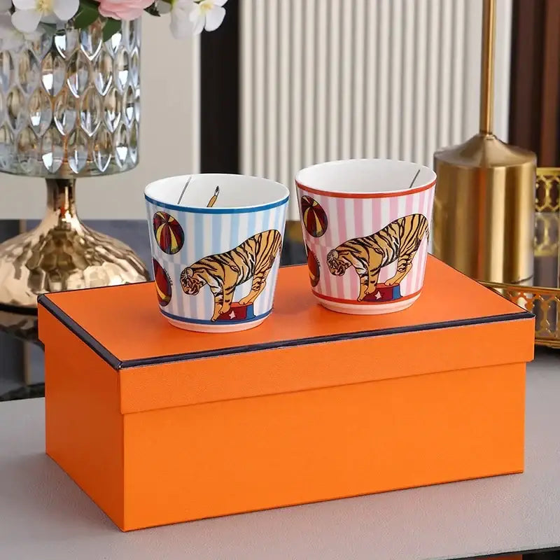 Two ceramic mugs in blue and white and pink and white stripes with tiger and circus ball designs from decorbites circus troup tableware set