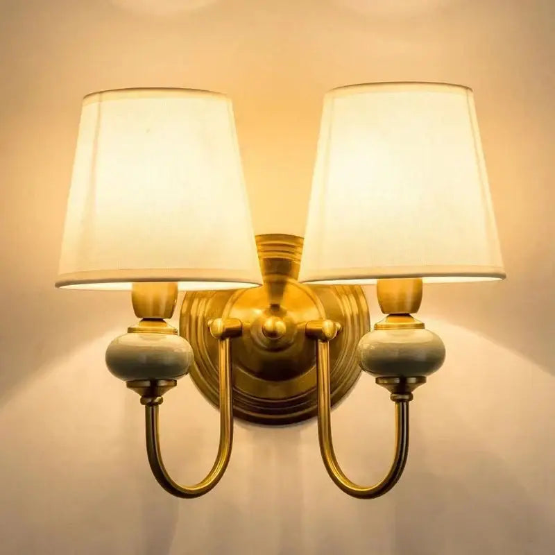 Brass-finished wall light with cream cloth cover shades and ceramic accents ideal for bedroom decorbites cloth cover wall use