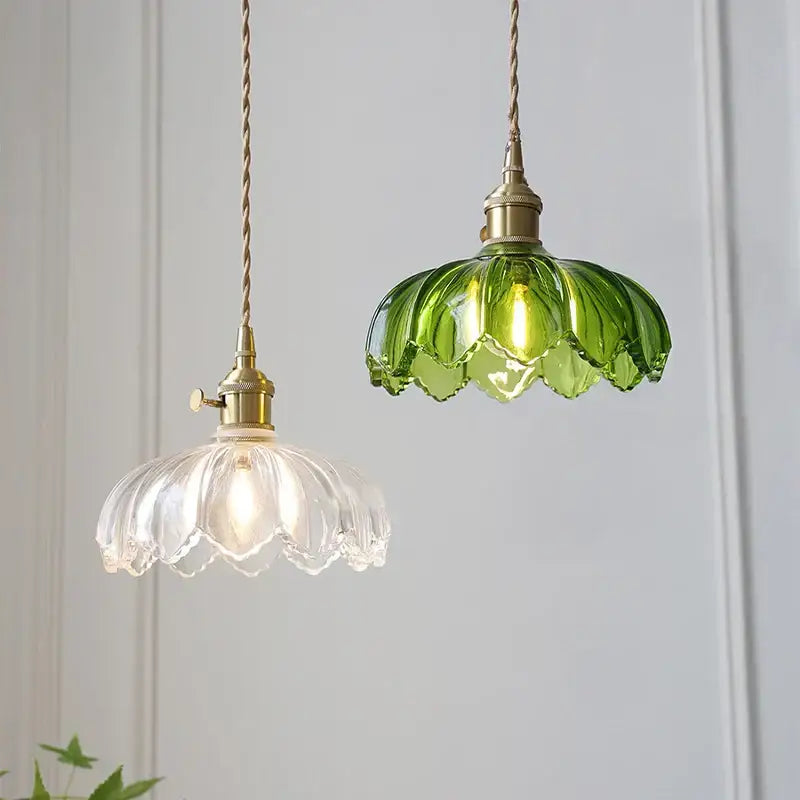 Two hanging pendant lights with classic glass petal and vibrant green designs, brass hardware, and twisted cords for dining rooms
