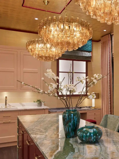 A tall glossy teal ceramic vase with textured surface on marble countertop complements decorbites large pink glass chandelier lighting