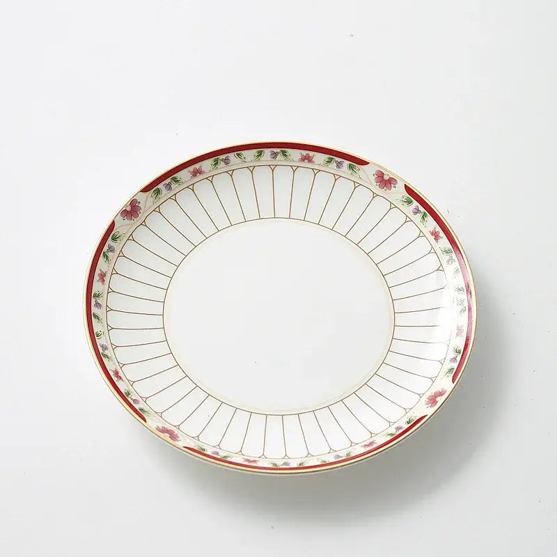A white ceramic saucer with a delicate red and gold floral border from a classical gold-striped ceramic cup and saucer set