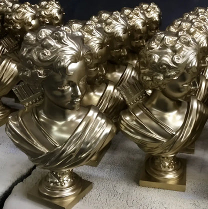 Golden metallic cupid statue plaster sculpture with intricate curly hair and draped fabric on ornate square bases