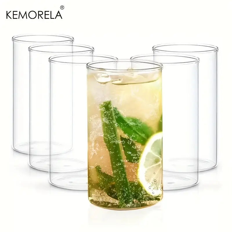 Clear cylindrical borosilicate drinking glasses set with one glass filled with a refreshing beverage garnished with mint and lime