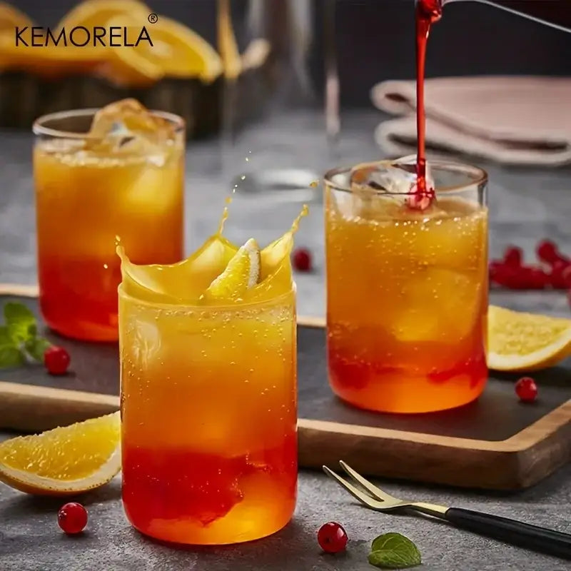 Clear borosilicate drinking glasses set featuring vibrant orange-red layered cocktails with ice and citrus garnishes