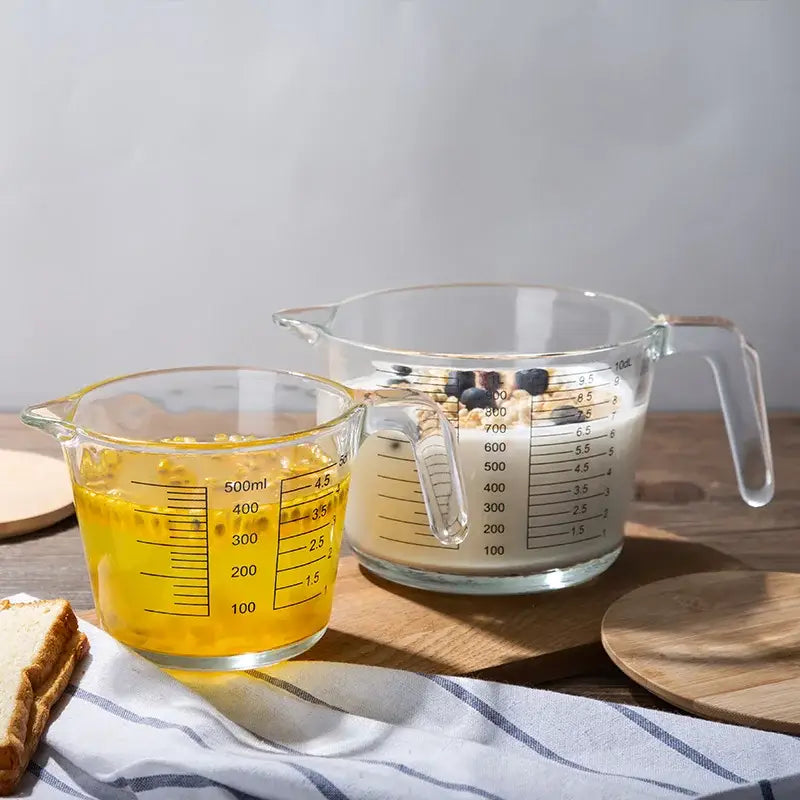 Clear borosilicate glass measuring cups with black markings filled with yellow liquid and milky mixture decorbites measuring cup