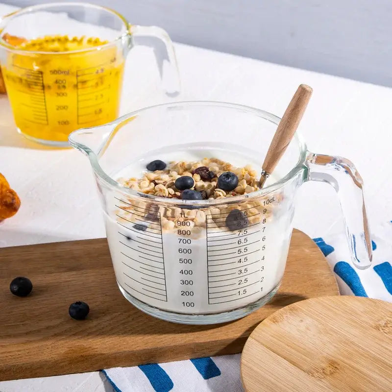 Clear borosilicate glass measuring cup with black markings filled with milk and granola and a wooden spoon inside decorbites borosilicate glass