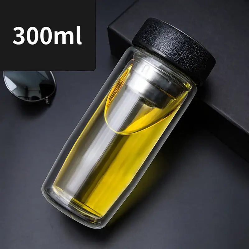 Clear double-walled glass travel mug with infuser black lid silver filter filled with golden liquid for thermal insulation decorbites double-deck glass cups