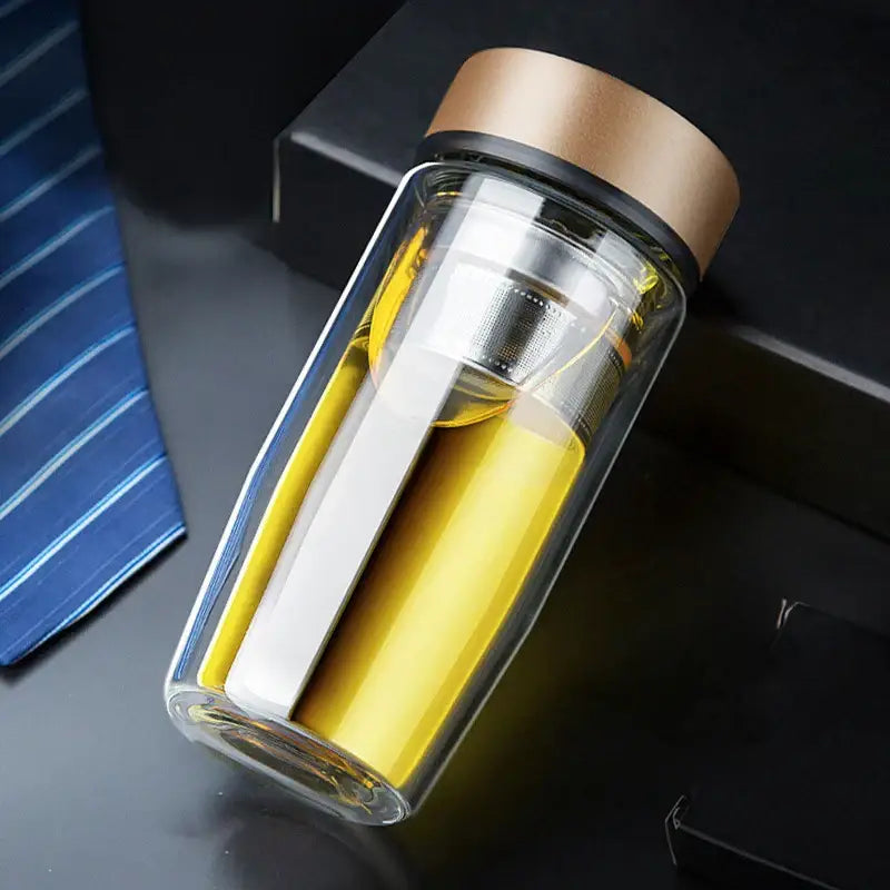 Clear double-walled glass travel mug with gold lid and stainless steel infuser filled with yellow liquid for thermal insulation decorbites double-deck glass cups
