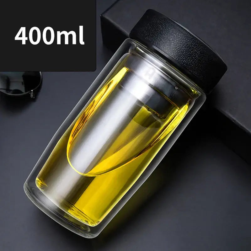 A clear decorbites double-deck glass travel mug with black lid filled with golden liquid showcasing thermal insulation