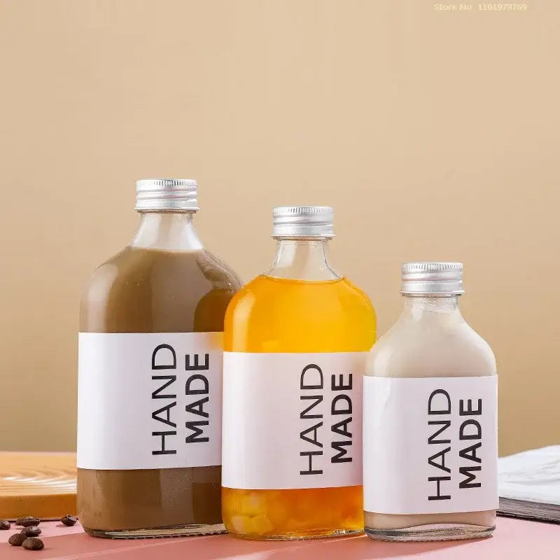 Three clear glass beverage bottles with silver caps and handmade labels filled with colorful liquids for kitchen juicing set