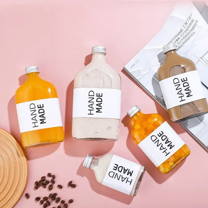 Four decorbites clear glass beverage bottles with silver caps and handmade labels filled with colored liquids for kitchen juicing