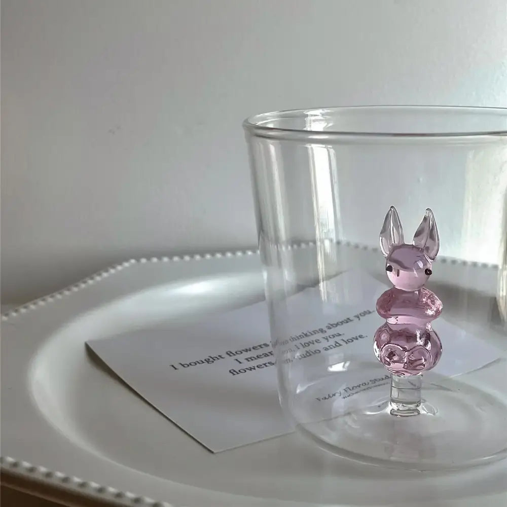 A translucent pink glass bunny figurine with black bead eyes on a clear glass base for decorbites cactus bunny drinkware