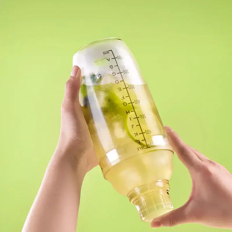Clear glass cocktail shaker with silver lid filled with ice and green liquid by decorbites cocktail shaker for barware