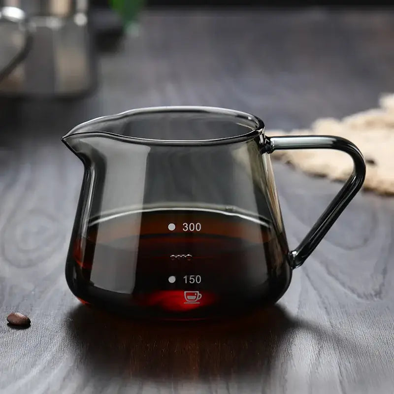 A sleek dark-tinted glass coffee pot with black handle and measurement markings for 150ml and 300ml