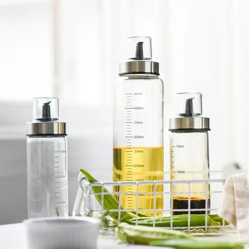 Clear glass condiment bottle set with silver caps black pumps and milliliter measurements for kitchen use