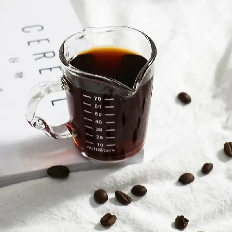 Clear glass espresso measuring cup with handle and white milliliter markings filled with dark coffee