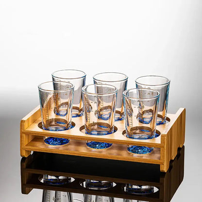 Set of six decorbites clear glass liquor cups with blue-tinted bases and measurement markings in a wooden rack