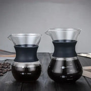 Two clear glass pour over coffee makers with black silicone bands and stainless steel filters filled with brewed coffee