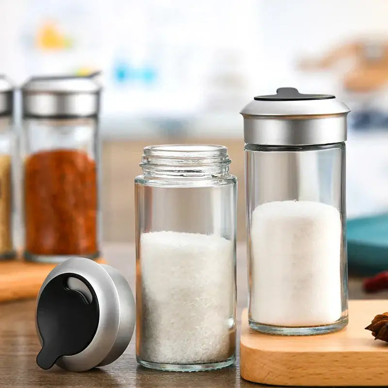 Clear glass rotating spice jar set with sleek silver lids including one filled with white granulated sugar for seasoning