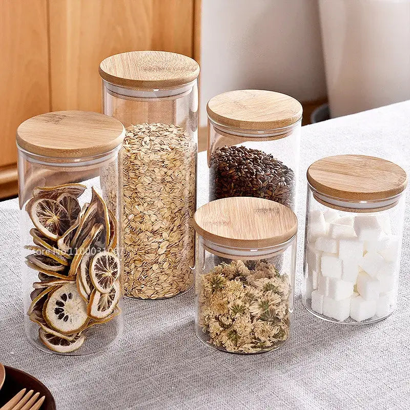 Clear glass storage jars with natural bamboo lids holding various dry pantry items for kitchen organization