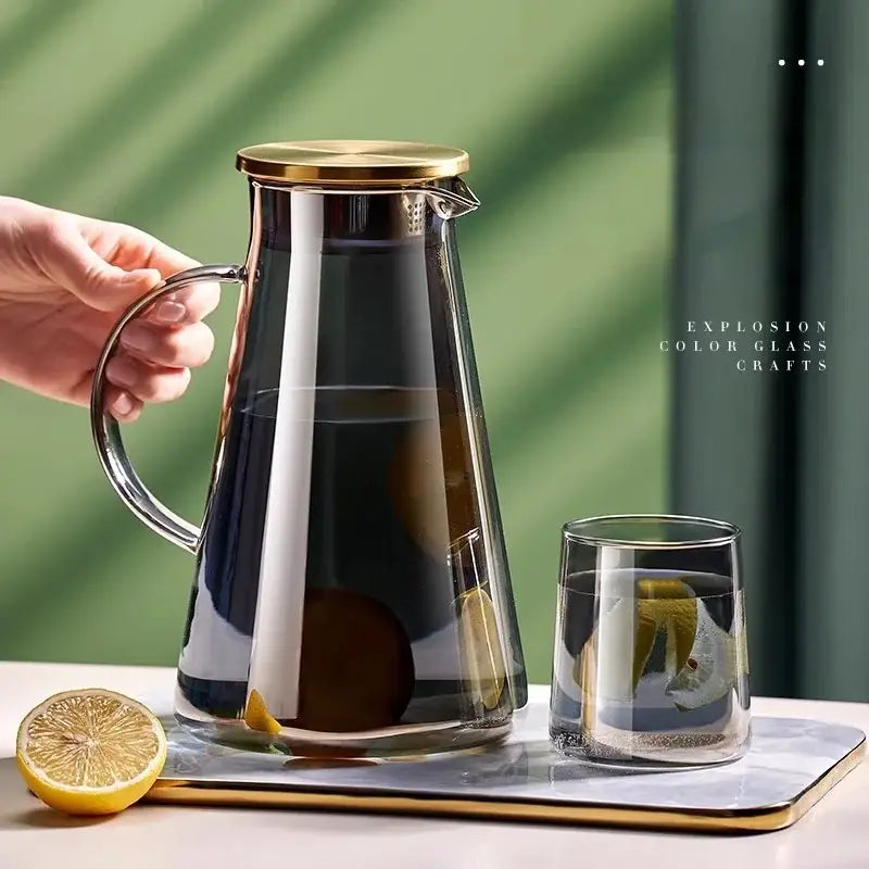 A sleek dark-tinted glass juice kettle with gold-toned lid and handle filled with lemon water from decorbites kettle set