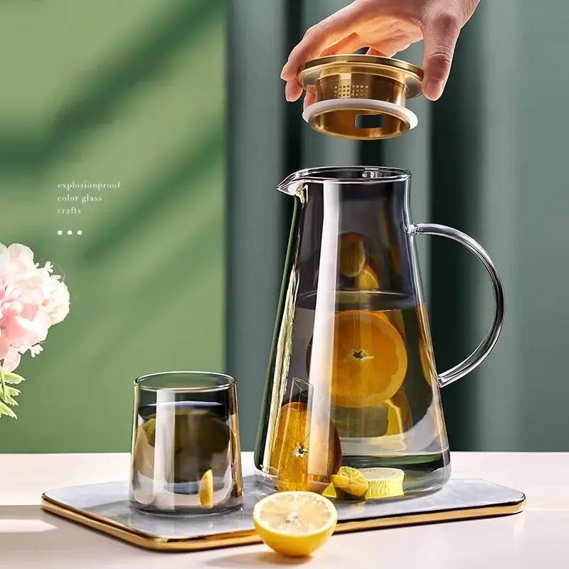 Clear gold glass juice kettle set featuring a clear glass pitcher with gold-toned lid and handle filled with sliced citrus