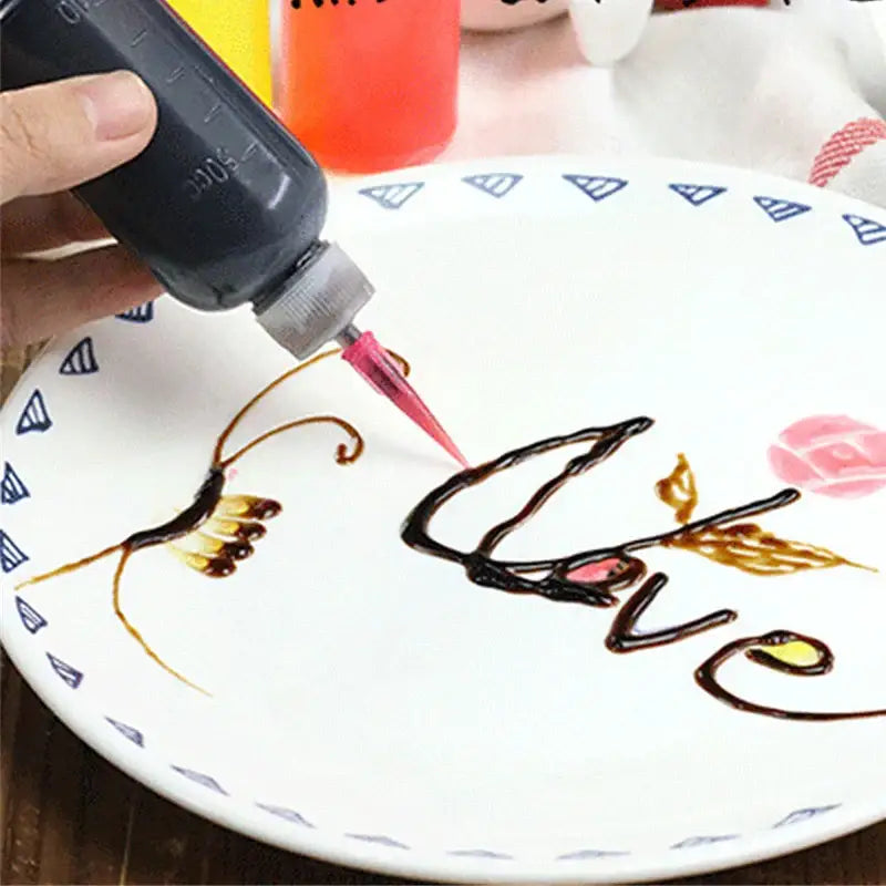 Clear plastic cake decor squeeze bottles with pink-tipped nozzle used to write love in chocolate syrup on white plate