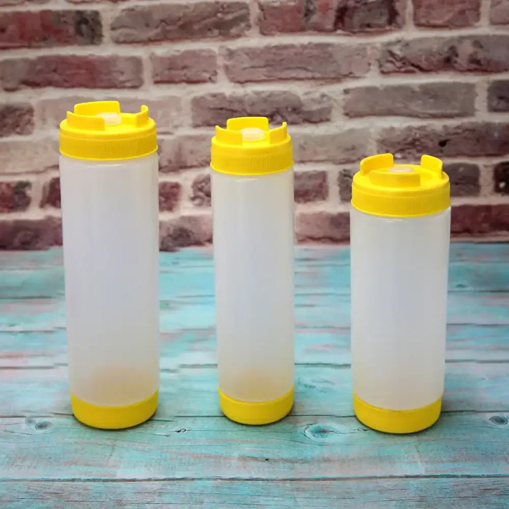 Three translucent plastic tomato squeeze bottles with bright yellow caps and bases in a kitchen set