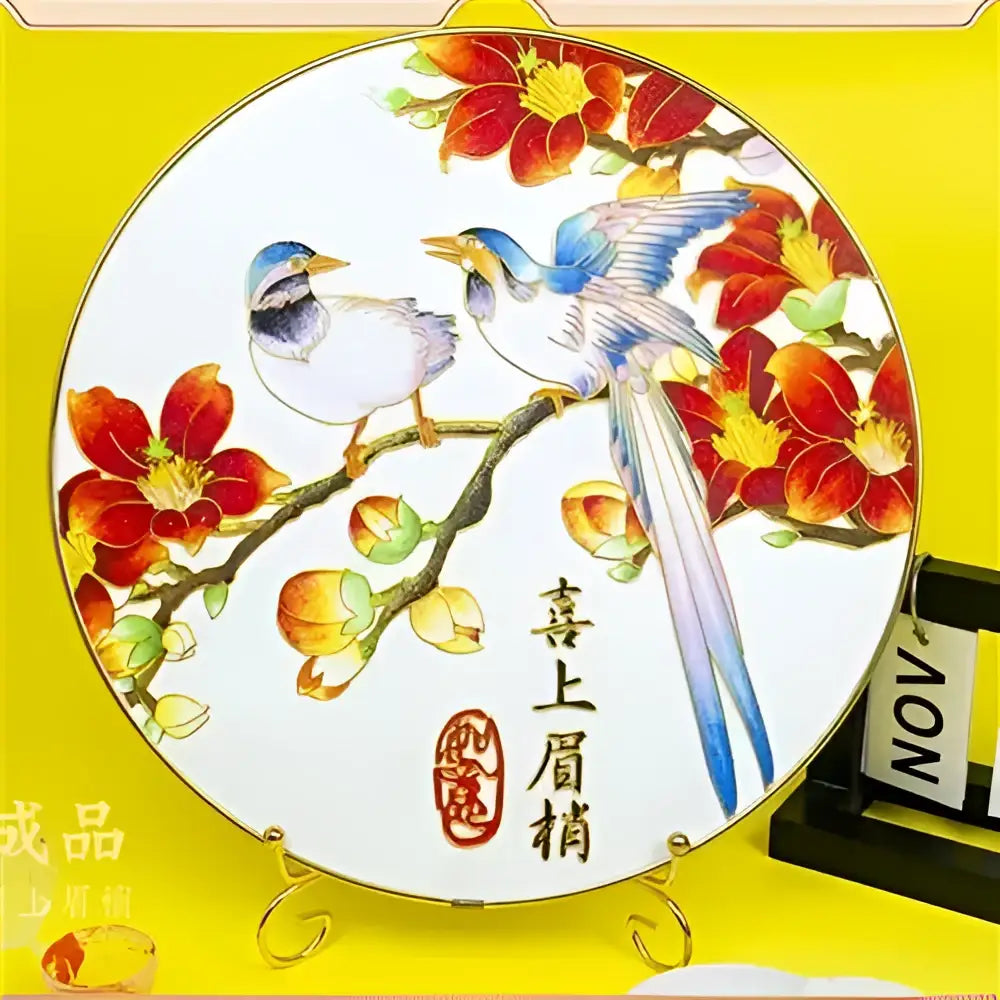 A round white ceramic plate with hand-painted blue and red birds and gold trim in a decorbites cloisonne silk enamel diy kit