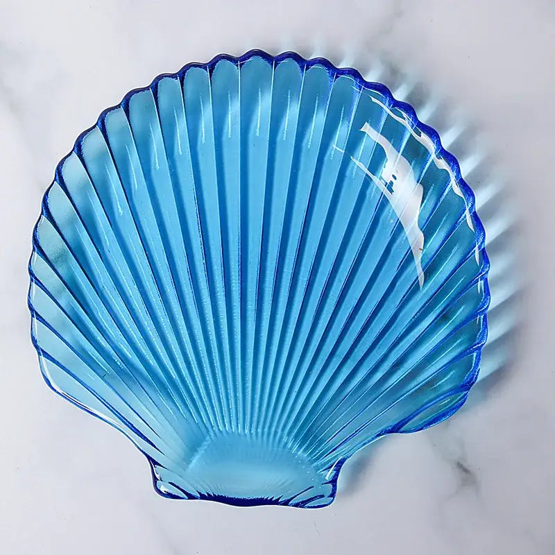 Translucent blue glass dish plate shaped like a scallop shell with ridged grooves and a glossy finish for dining use