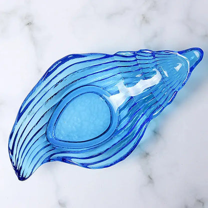 Translucent blue glass dish plate saucer shaped like a seashell with ridged wavy lines and an oval indentation