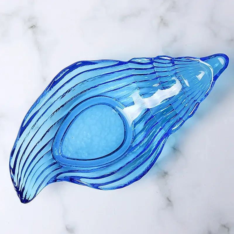 Translucent blue glass dish plate saucer shaped like a seashell with ridged wavy lines and an oval indentation