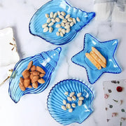 Coastal blue glass dish plate saucer set shaped like seashells and starfish holding assorted nuts and snacks