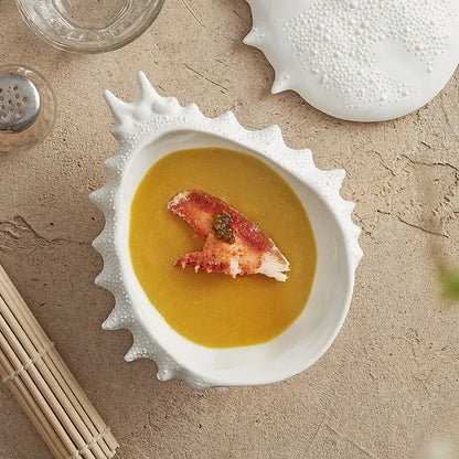 Coastal white ceramic soup bowl with shell shape and textured edges holding yellow soup with lobster claw garnish