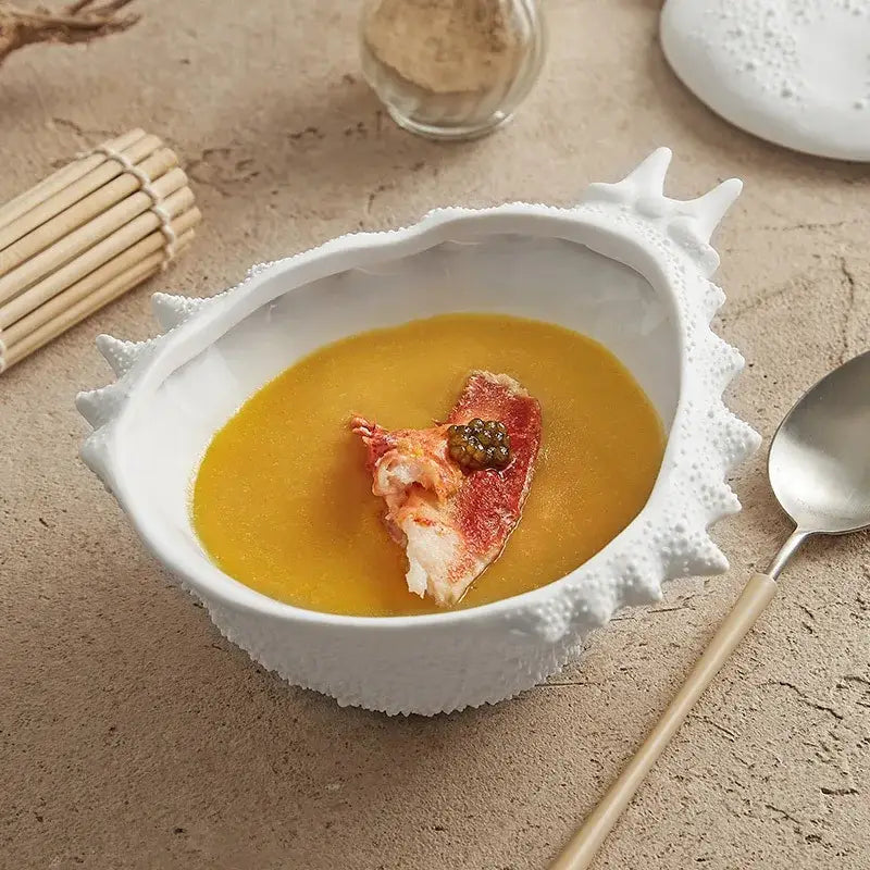 Coastal white ceramic soup bowl shaped like a shell filled with golden soup and lobster tail topper