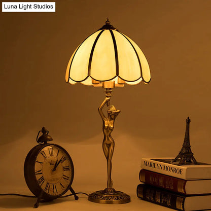 Lámpara de mesa colonial de cristal beige con dos cabezales dorados, diseño festoneado y elegante base con forma de mujer desnuda.