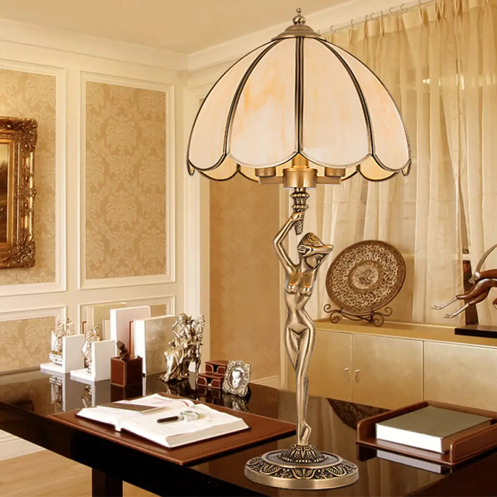 Lámpara de mesa colonial de cristal beige con dos cabezales dorados, diseño festoneado y elegante base con forma de mujer desnuda.