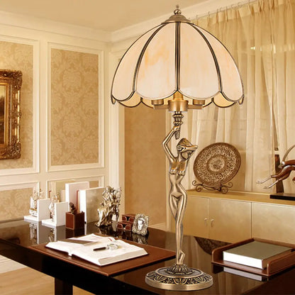 Lámpara de mesa colonial de cristal beige con dos cabezales dorados, diseño festoneado y elegante base con forma de mujer desnuda.