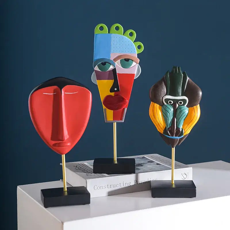 Three colorful african abstract face monkey sculptures with bold geometric designs on gold stands for living room decorbites decor
