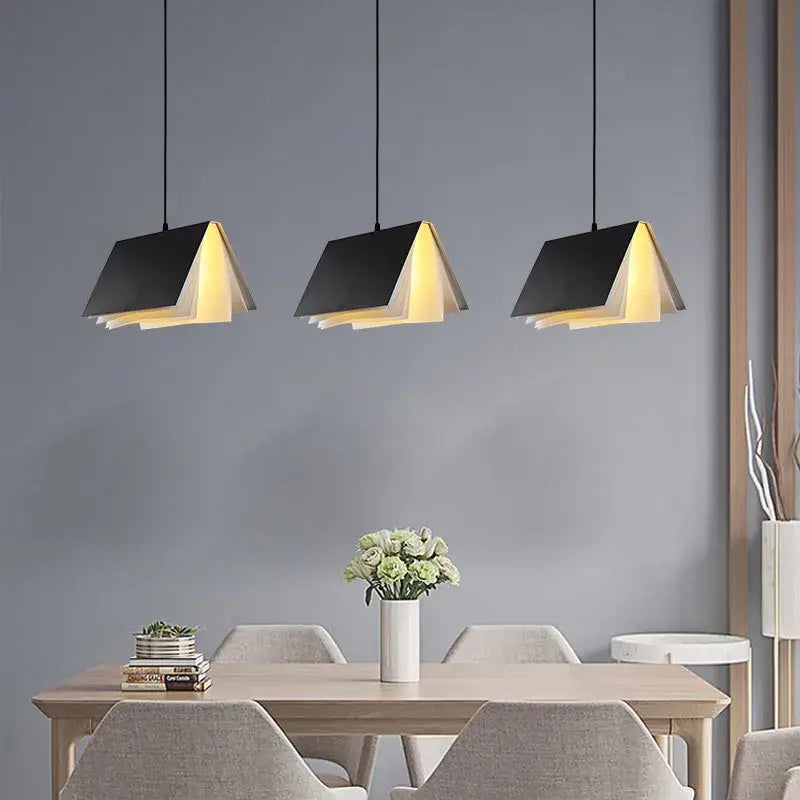 Three black colorful book pendant lamp with warm yellow interior lighting hangs above a dining table decorbites book pendant