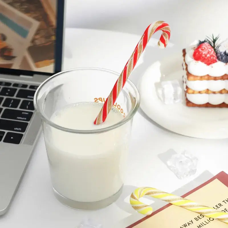 A colorful christmas long handle candy cane glass stirring stick in red and gold stripes in a clear glass of milk
