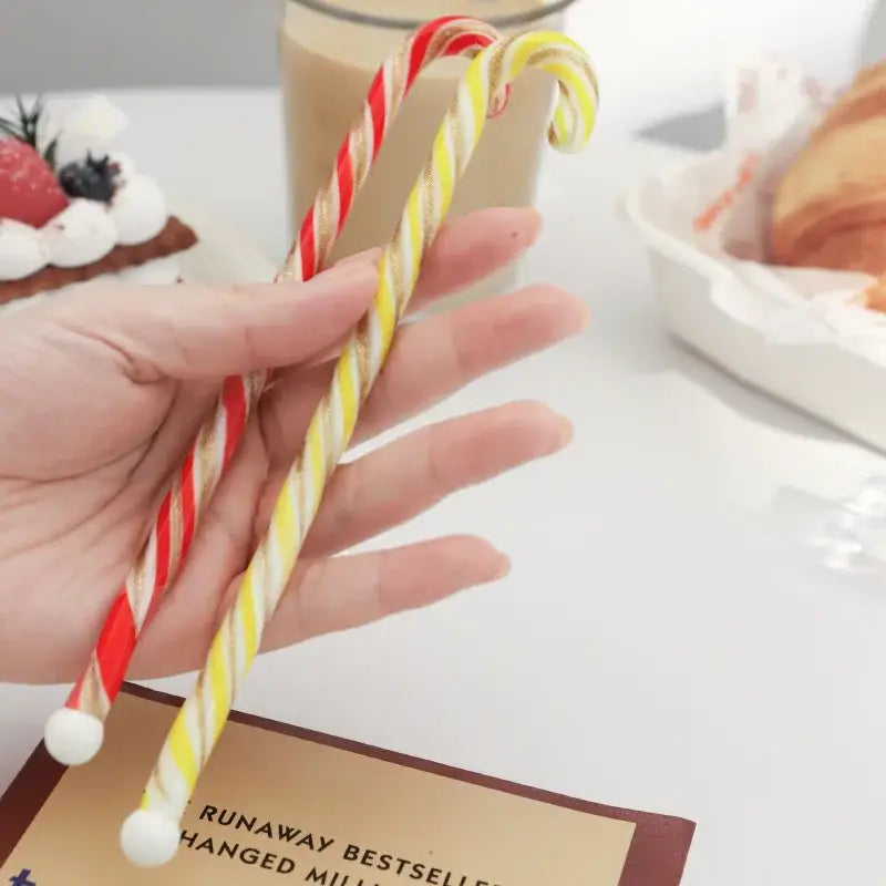 Two colorful christmas long handle candy cane glass stirring sticks with red white and yellow white stripes ending in white balls