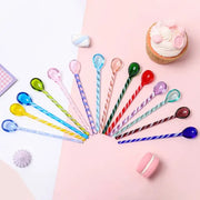 A set of colorful glass stirring spoons with translucent bowls and striped handles arranged in a fan shape by decorbites colorful glass