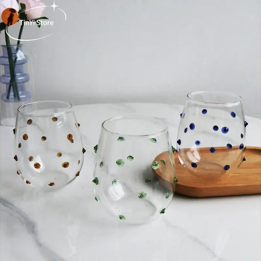 Three clear stemless wine glasses with colorful glass wave dots and decorative beads in gold green and blue