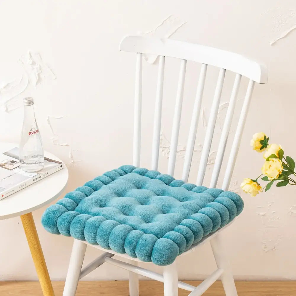 A teal quilted cookie biscuit cushion with tufted rounded edges on a white wooden chair for living room use