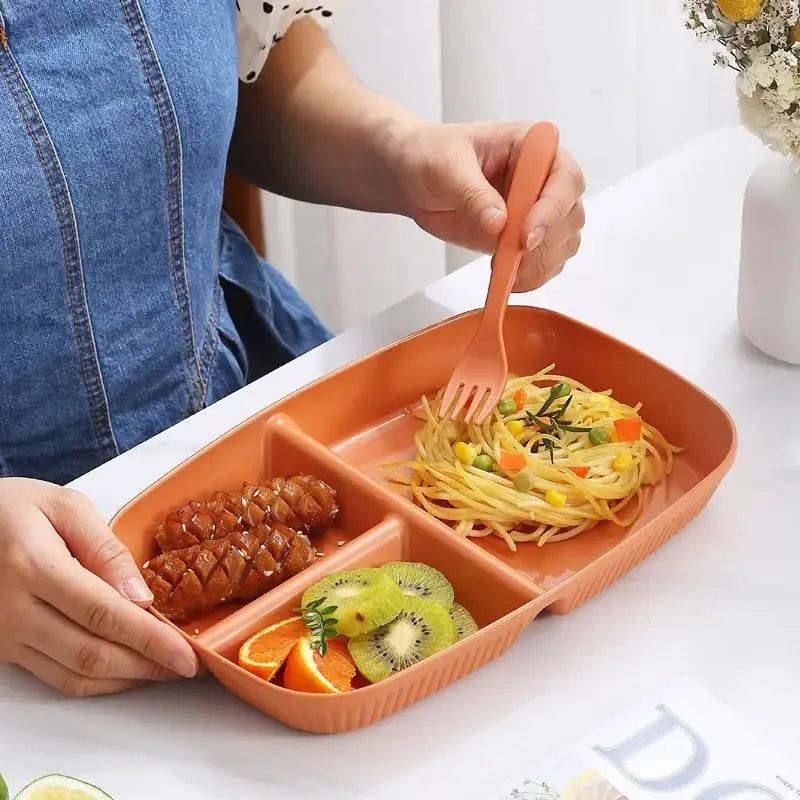 Orange plastic ribbed divided dish diet plate with three compartments holding pasta sausage and fruit slices